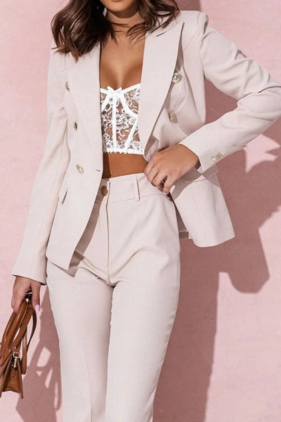 Woman wearing a light gray suit with a lace top against a pink background
