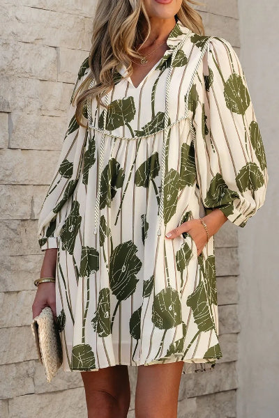 Woman wearing a white dress with green leaf pattern against a stone wall.