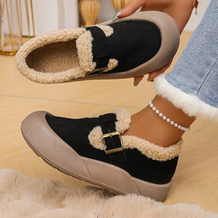 Pair of black and beige slippers with a buckle held by a person wearing denim jeans.