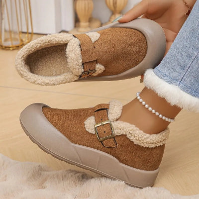 Brown and beige slip-on shoes with fur trim worn by a person indoors.