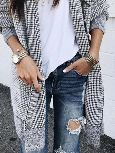 Person wearing a checkered coat, white shirt, and ripped jeans against a white wall.