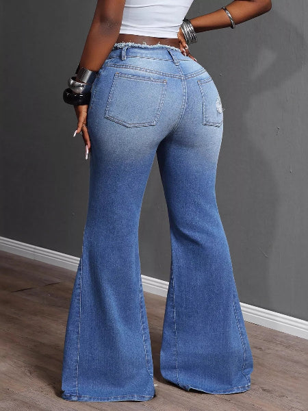 Person wearing blue flared jeans against a gray wall.
