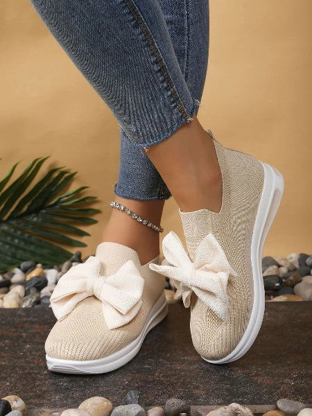Beige slip-on shoes with large bows worn with blue jeans on a natural background