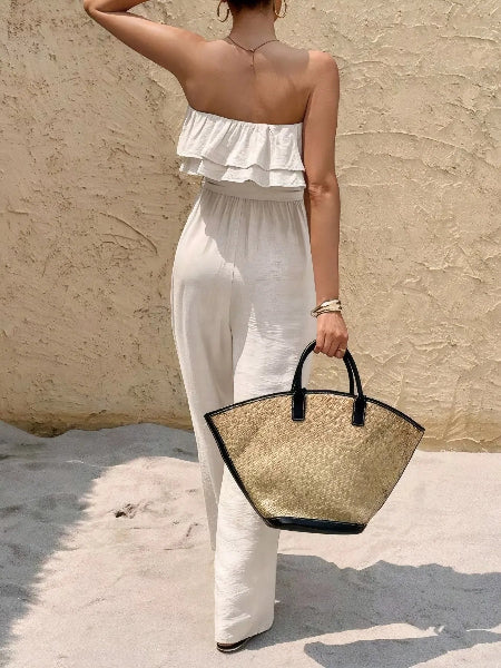 Woman in a white outfit holding a straw bag against a beige wall.