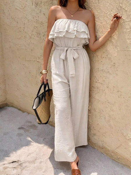 Woman wearing a white strapless jumpsuit against a textured wall.