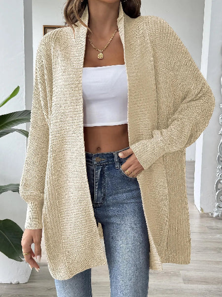Person wearing a beige cardigan over a white top and blue jeans indoors.