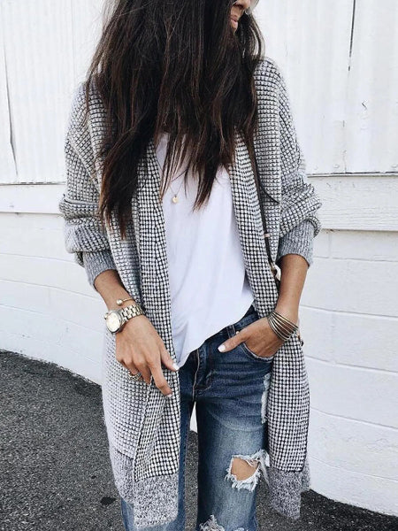 Person wearing a plaid coat, white shirt, and ripped jeans against a white wall.