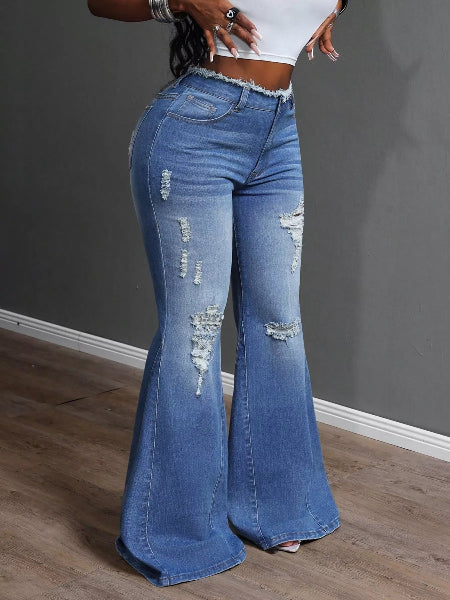 Person wearing blue flared jeans with a white top against a gray wall.